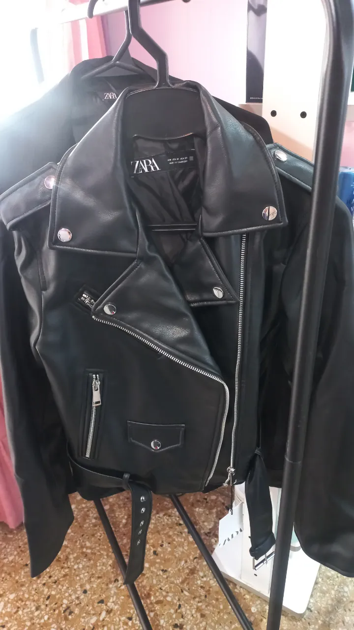 Campera de cuero sintético negra con cierre cruzado, cuello solapa con botones a presión, cinturón y bolsillos con cierre.