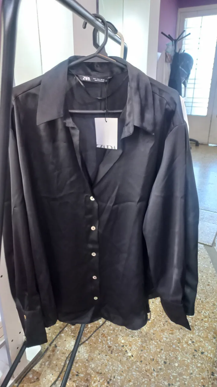 Camisa negra de seda con botones blancos nacarados. Cuello camisero y mangas largas con puños.