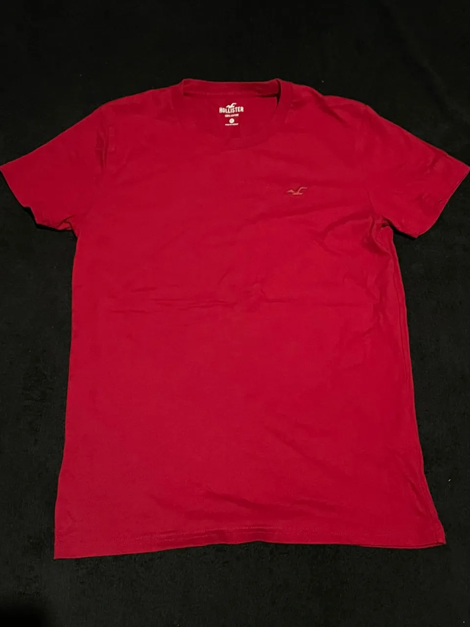 Remera roja lisa con logo pequeño bordado en el frente.