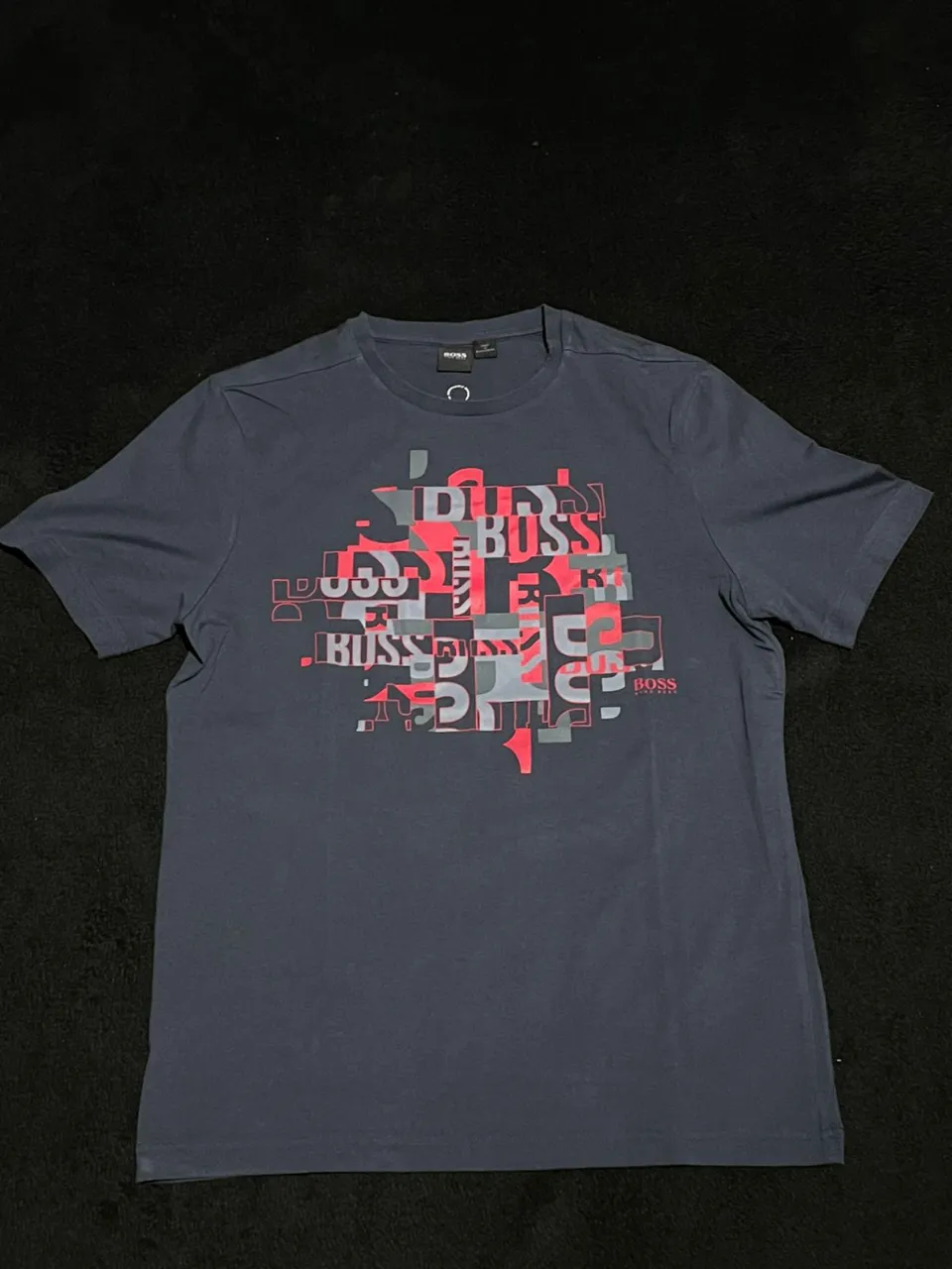 Remera de manga corta de color azul marino con estampa abstracta de letras y formas geométricas en tonos rojo y gris. Posee el logo de la marca en la parte inferior derecha de la estampa.