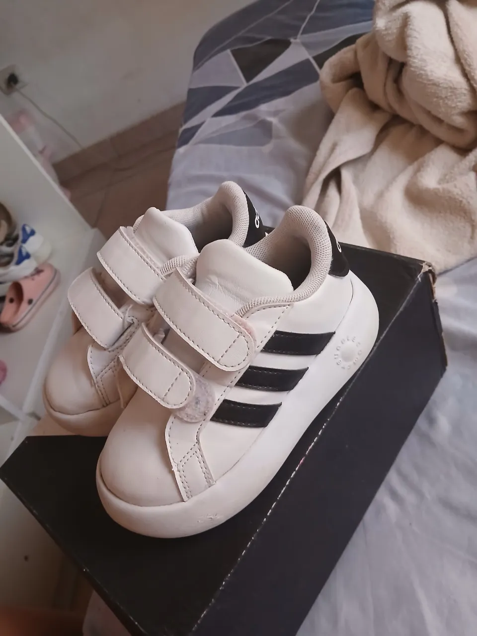 Zapatillas blancas con detalles negros y abrojo. Tienen tres tiras negras a los costados y el logo de la marca en la parte trasera.