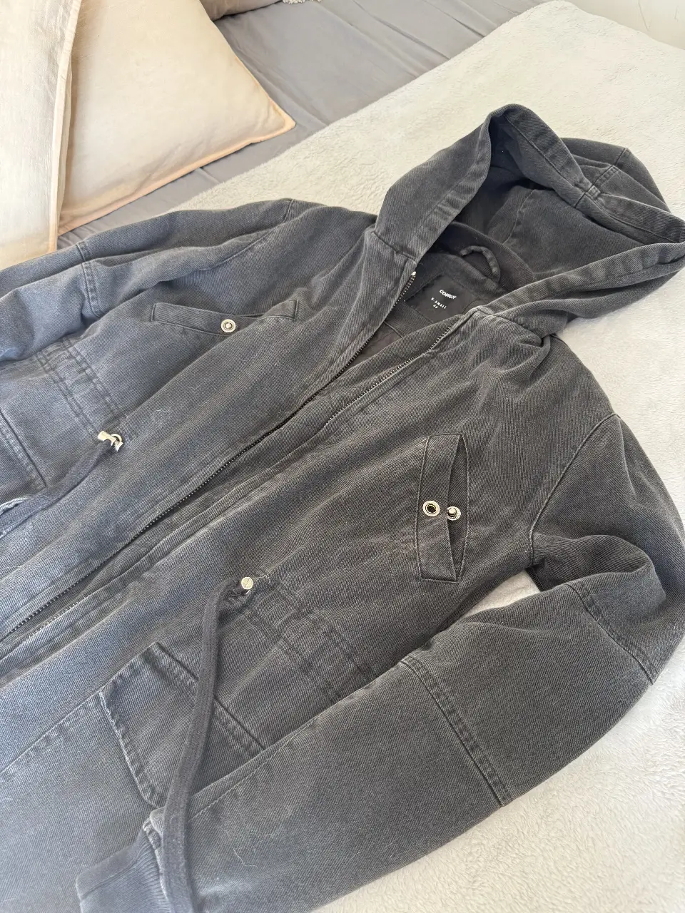 Parca larga con capucha de jean, color gris oscuro, casi negro, con cierre y bolsillos. Ideal para un look casual y canchero. Complot talle XS. 