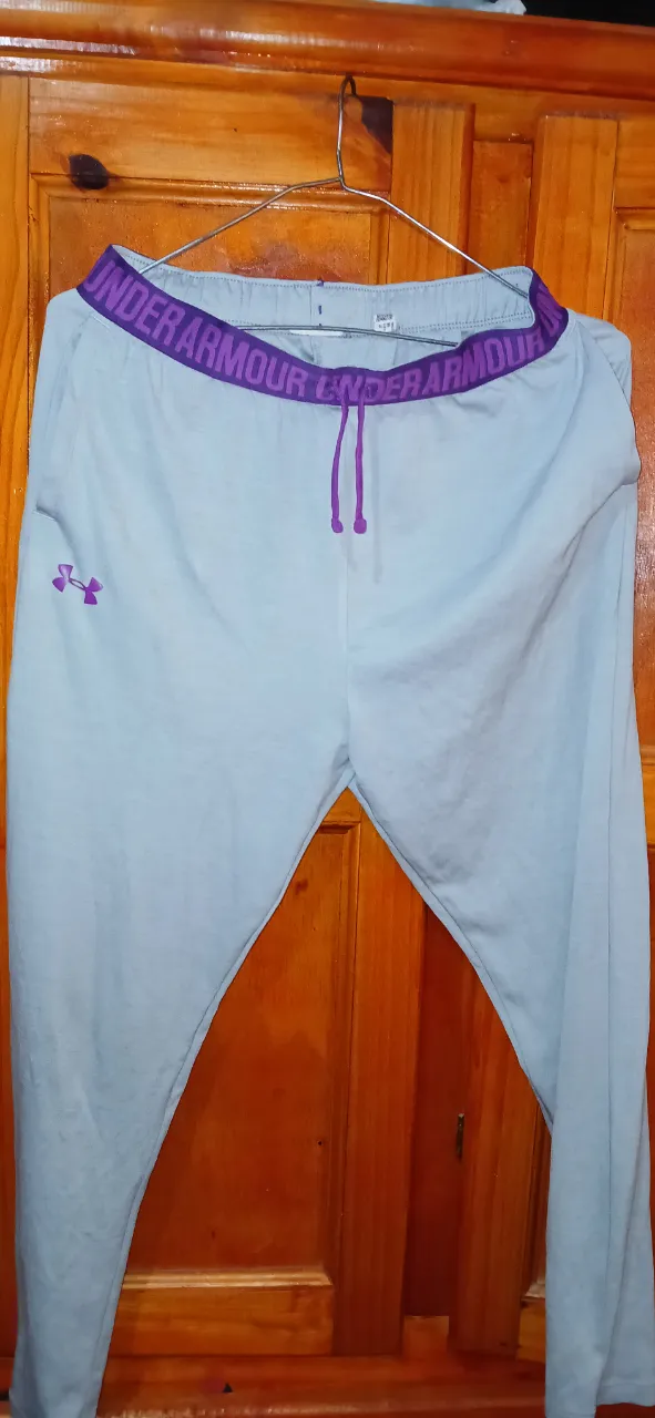 Pantalón deportivo suelto de mujer, color celeste con cintura violeta y logo Under Armour. Ideal para actividades físicas o uso casual.
