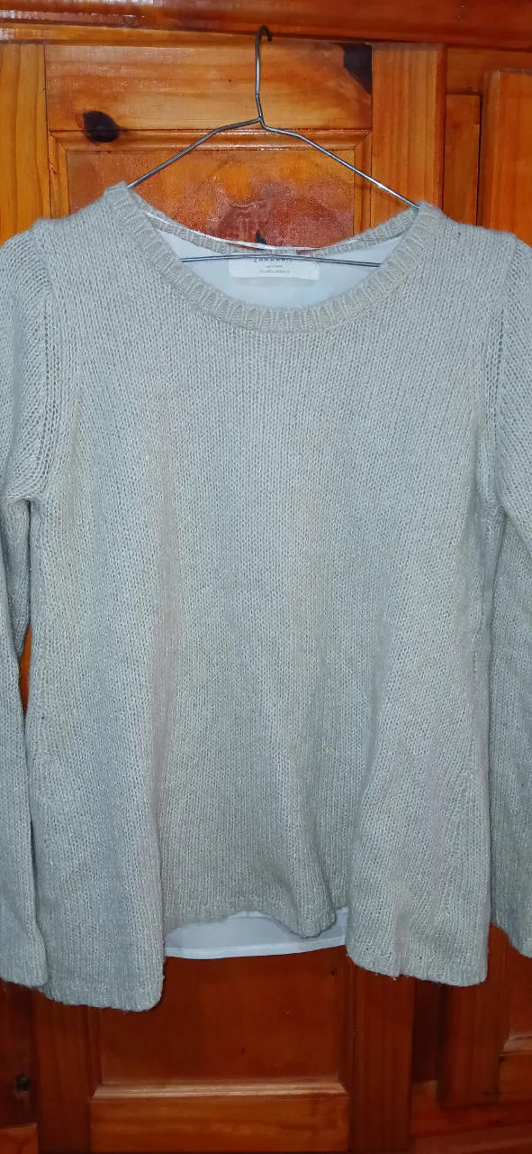 Sweater largo de punto, color gris claro. Cuello redondo y mangas largas. Diseño con abertura en la espalda.