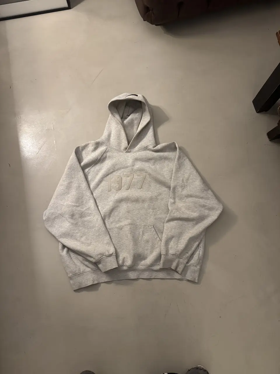 Buzo canguro de hombre, color gris con el número 1977 en relieve en el frente. Ideal para un look casual y cómodo.