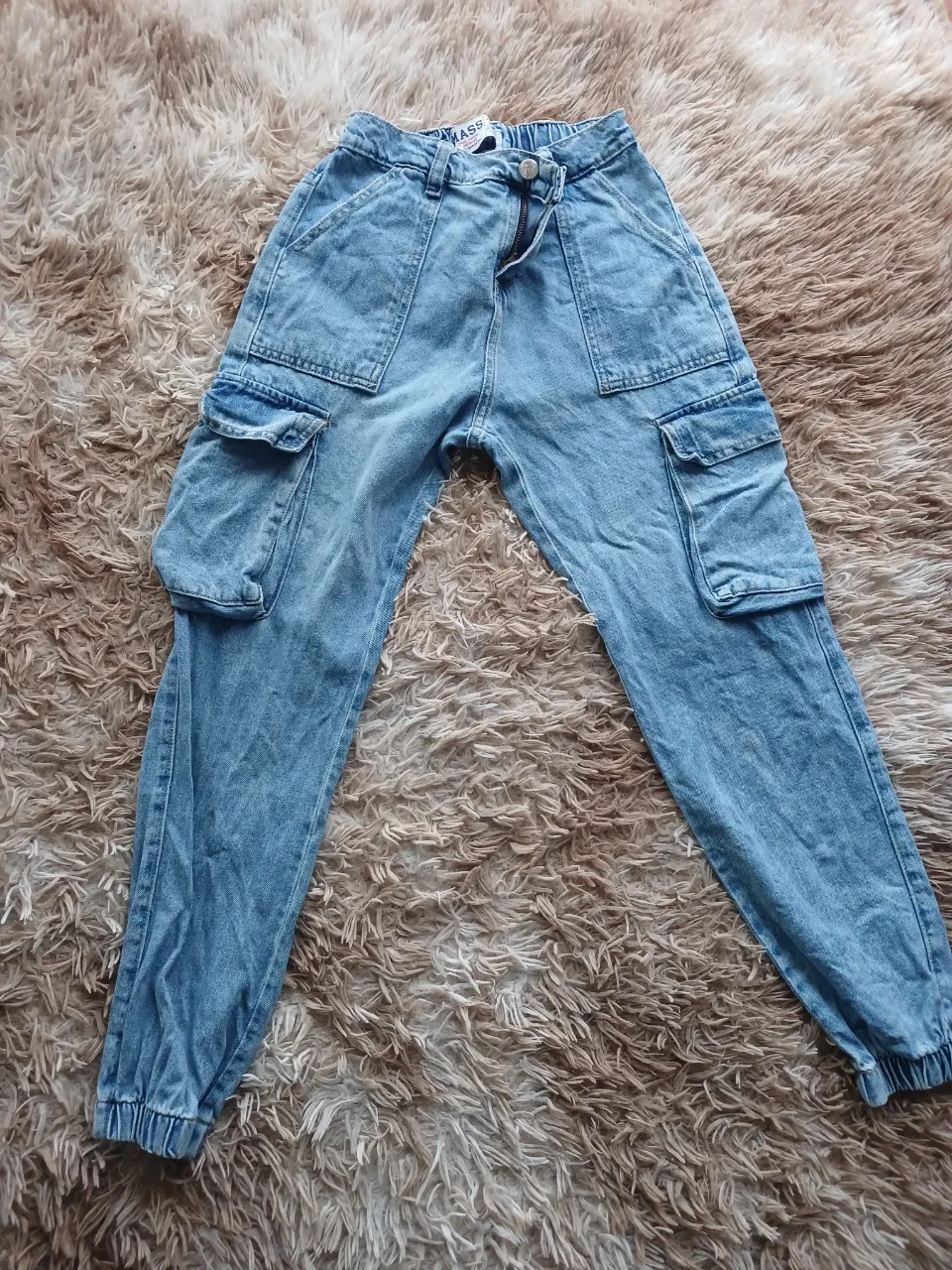 Pantalón cargo de jean azul claro, con bolsillos amplios y detalles utilitarios. Tiro alto y corte relajado, ideal para un look casual y moderno. Talle 14 en etiqueta, aplica para talle 12.