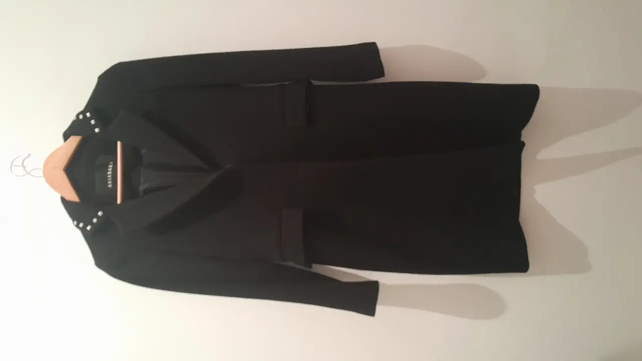 Tapado negro de paño con detalles de tachas en el cuello. Ideal para un look elegante y sofisticado.