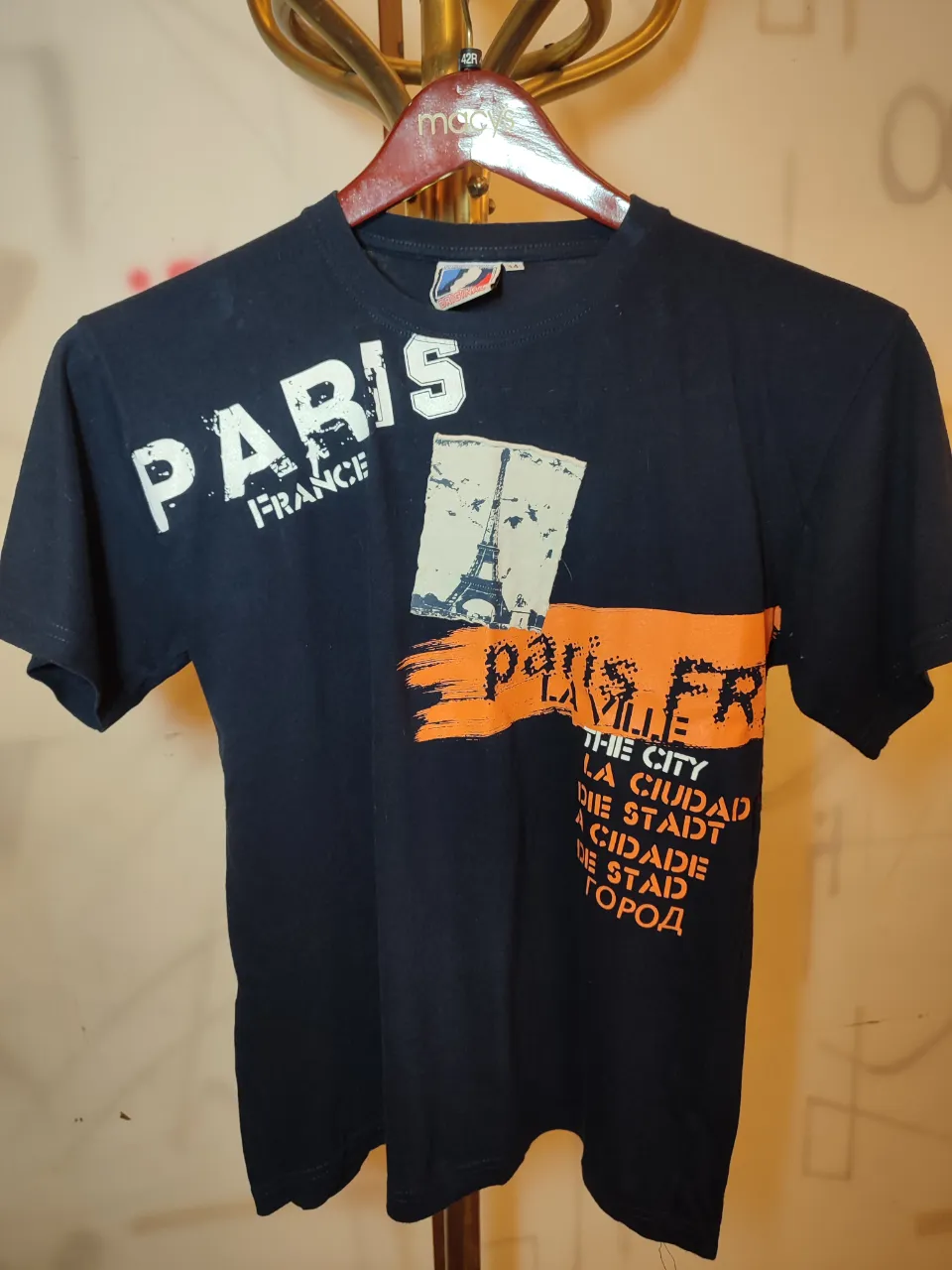 Remera de algodón negra con estampa "PARIS FRANCE" en blanco y naranja. La estampa incluye una imagen de la Torre Eiffel y texto en francés e inglés.marcado talle 14 Pero es un s/m .Ancho de hombros 0,46.Ancho de sisa 0,50.Largo 0,61