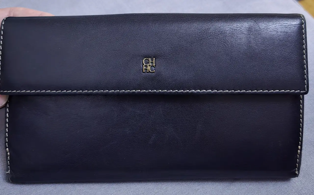 Billetera de cuero negro con el logo de la marca CH Carolina Herrera en dorado. Diseño elegante y funcional, ideal para llevar tus esenciales con estilo.