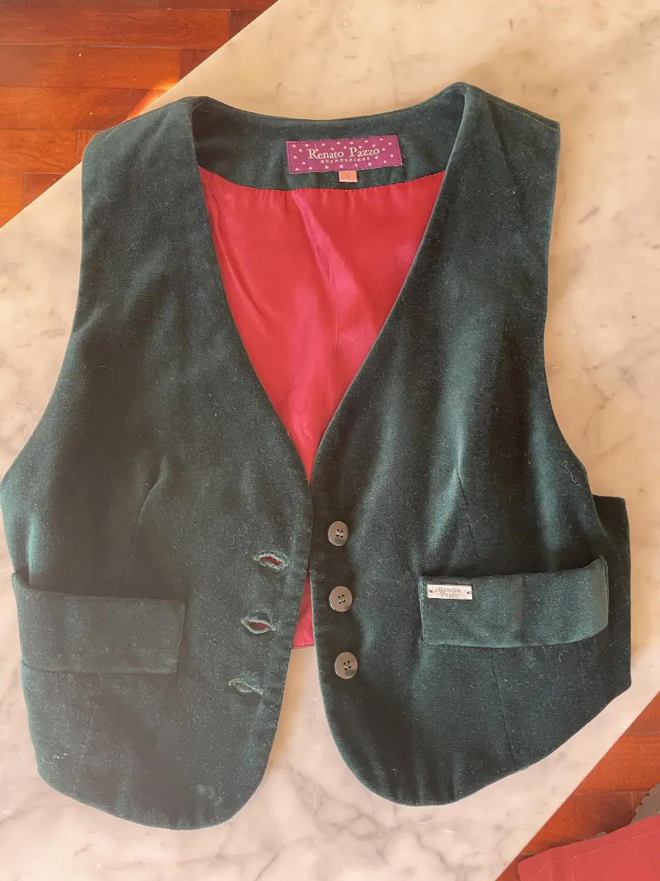 Chaleco de terciopelo verde oscuro con forro rojo. Detalles de botones y bolsillos. Ideal para un look elegante y sofisticado.