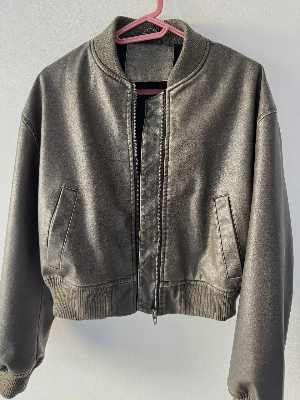 Campera bomber de cuero sintético en color gris verdoso. Ideal para un look casual y moderno. Cuenta con cierre frontal y bolsillos laterales. 