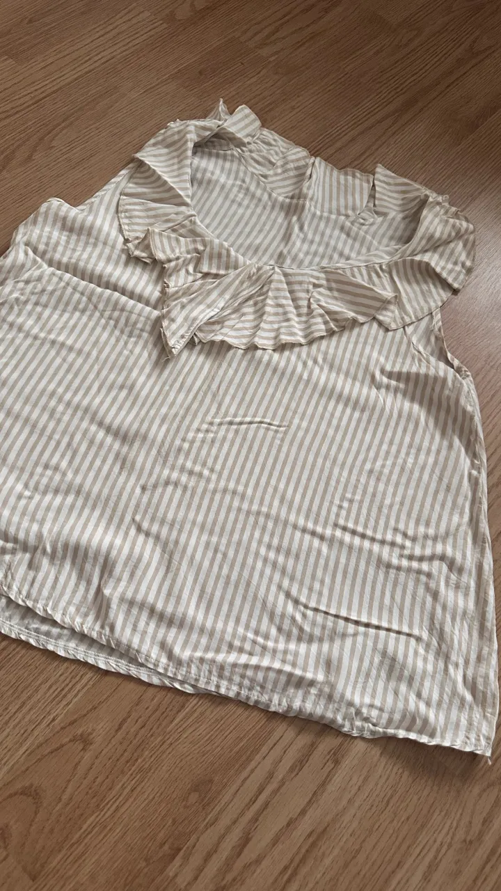 Musculosa blusa a rayas verticales blancas y beige con volados en el cuello y mangas.