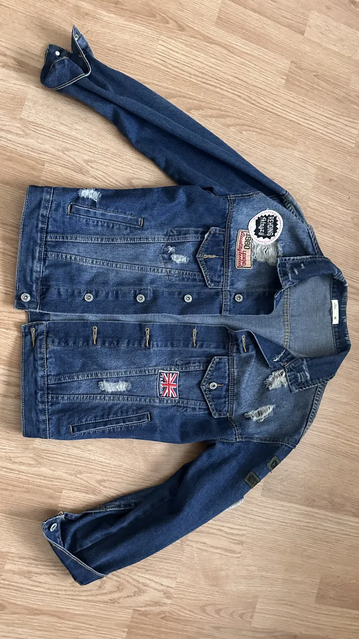 Campera de jean azul con parches y roturas. Tiene botones metálicos y bolsillos frontales con tapa.