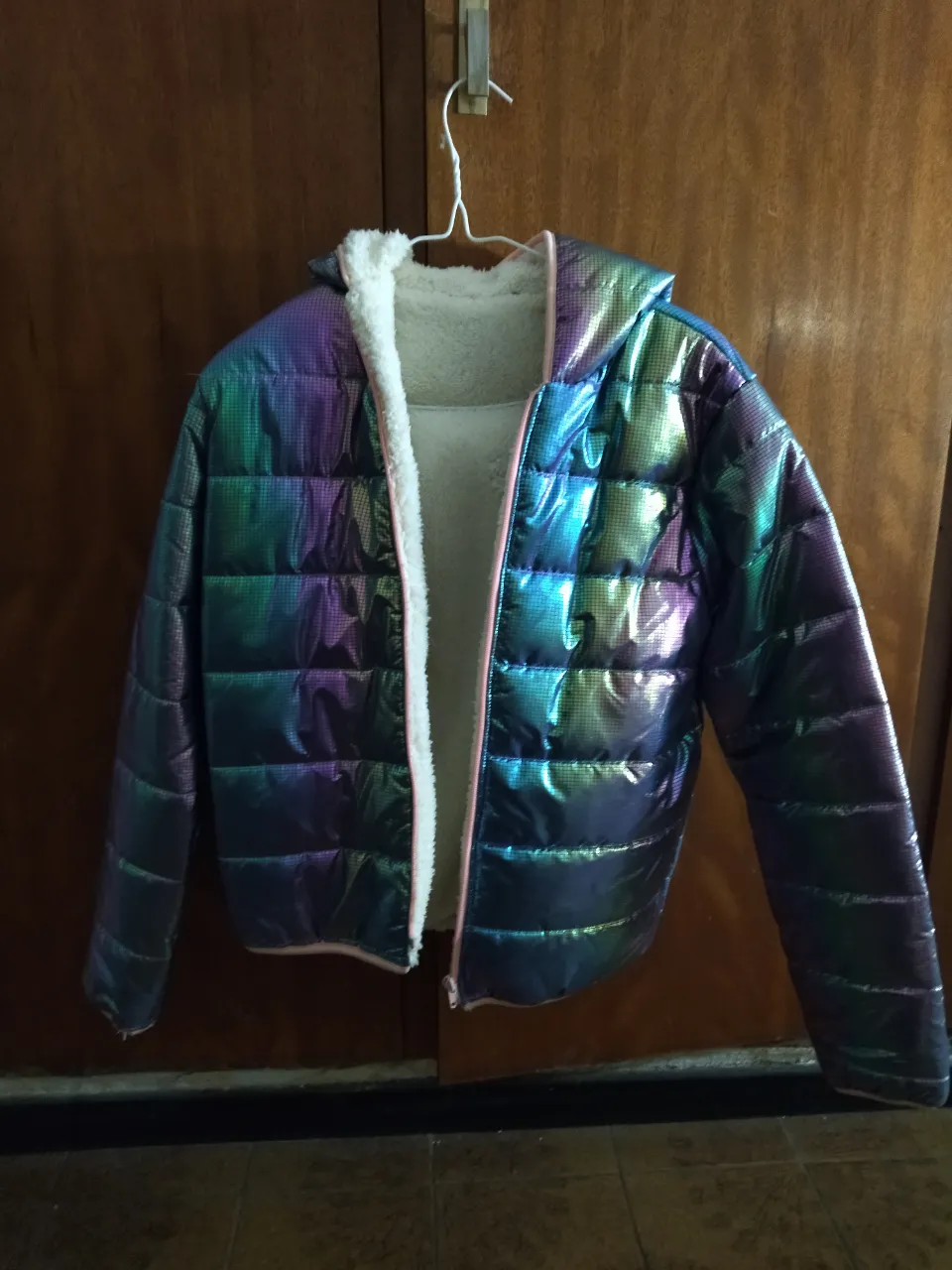 Campera acolchada con capucha, de diseño iridiscente en tonos azules, verdes y violetas. Posee forro interior de peluche blanco y cierre metálico.