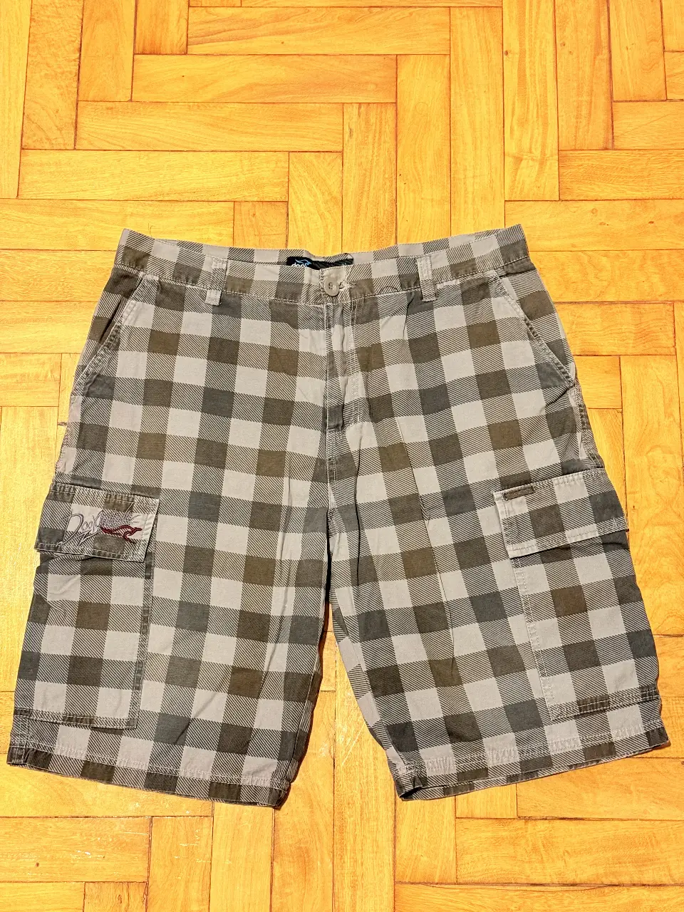 Short de hombre con estampado a cuadros en tonos grises y verdes. Diseño cargo con bolsillos laterales y traseros. Ideal para un look casual y cómodo.