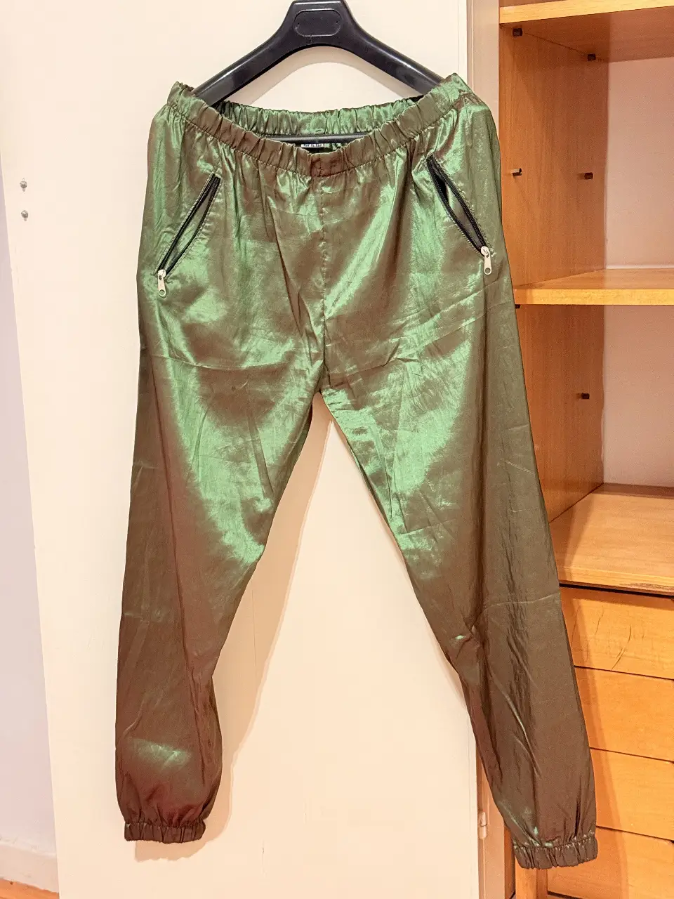 Pantalón suelto de mujer, color verde metalizado. Confeccionado en un tejido brillante, con cintura elastizada y bolsillos con cierre. Ideal para un look moderno y cómodo.