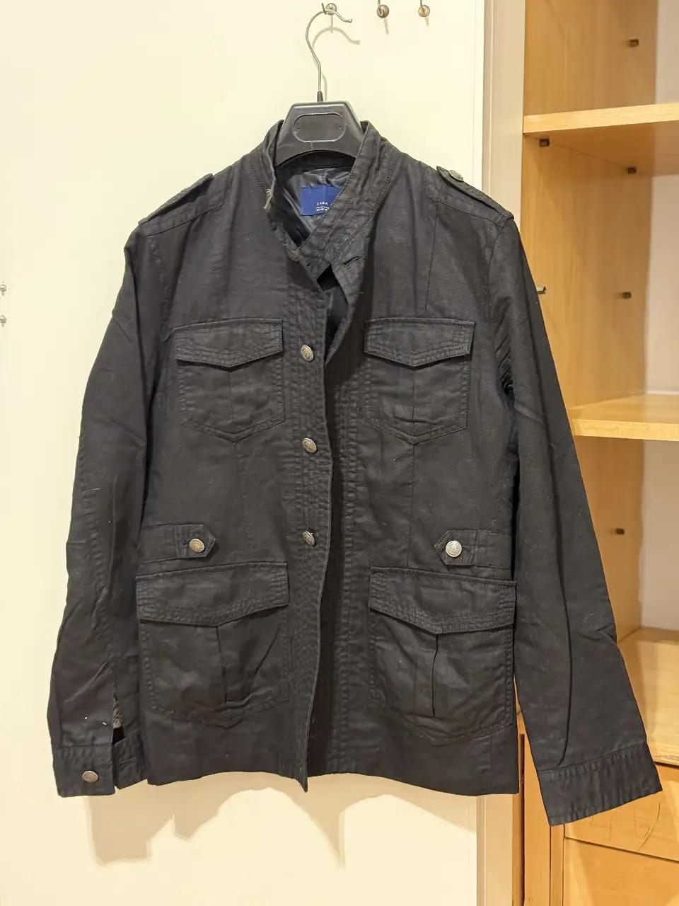 Campera negra Zara Man, estilo bomber con múltiples bolsillos, ideal para un look casual y urbano. Confeccionada en material resistente, perfecta para el día a día. Le falta un botón del hombro.