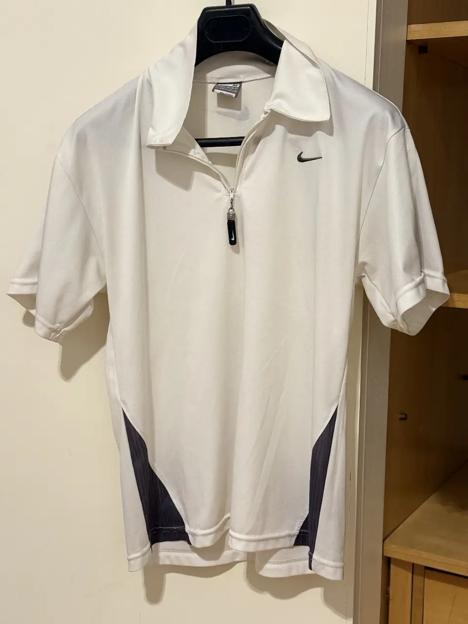 Remera deportiva Nike blanca con detalles en negro. Cuello polera con cierre, manga corta. Ideal para entrenar o usar en el día a día.