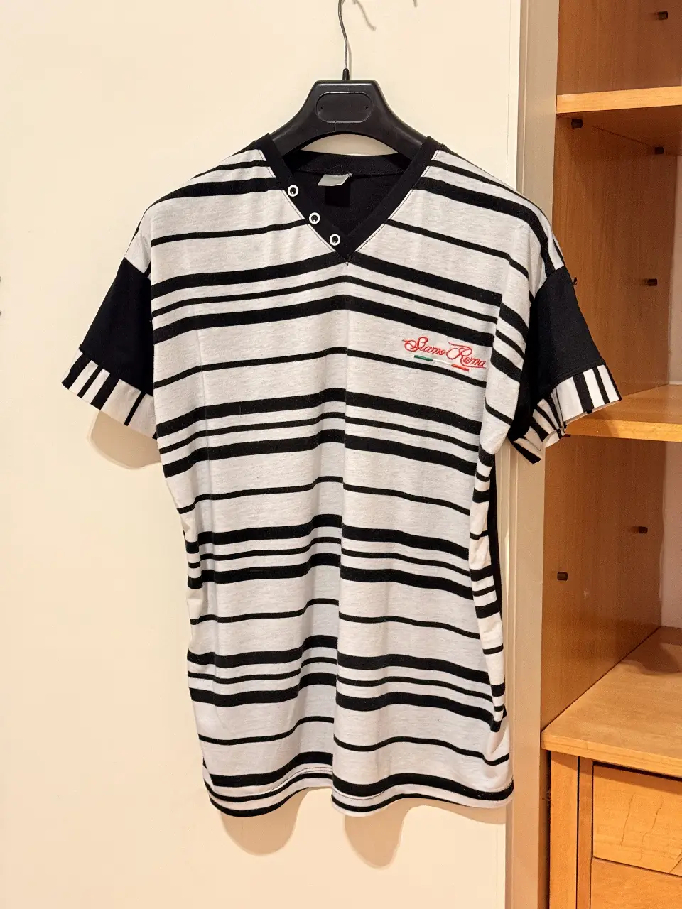Remera a rayas horizontales en blanco y negro, con detalles en negro en las mangas y cuello en V. Logo "Siamo Fuori" en rojo. Ideal para un look casual y con onda.
