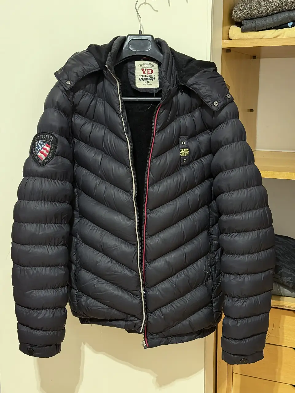 Campera de pluma negra para hombre, con capucha y cierre. Ideal para el invierno, con diseño acolchado en forma de zigzag. Cuenta con detalles como parches y un forro interior suave.