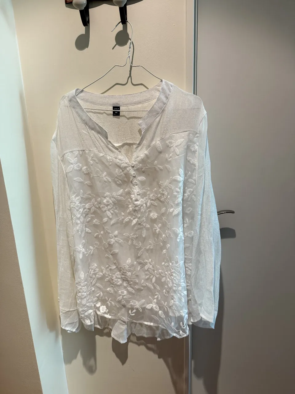 Blusa blanca con bordados florales en relieve y detalles de botones en el frente. Manga larga y escote en V sutil. Perfecta para un look delicado y romántico.