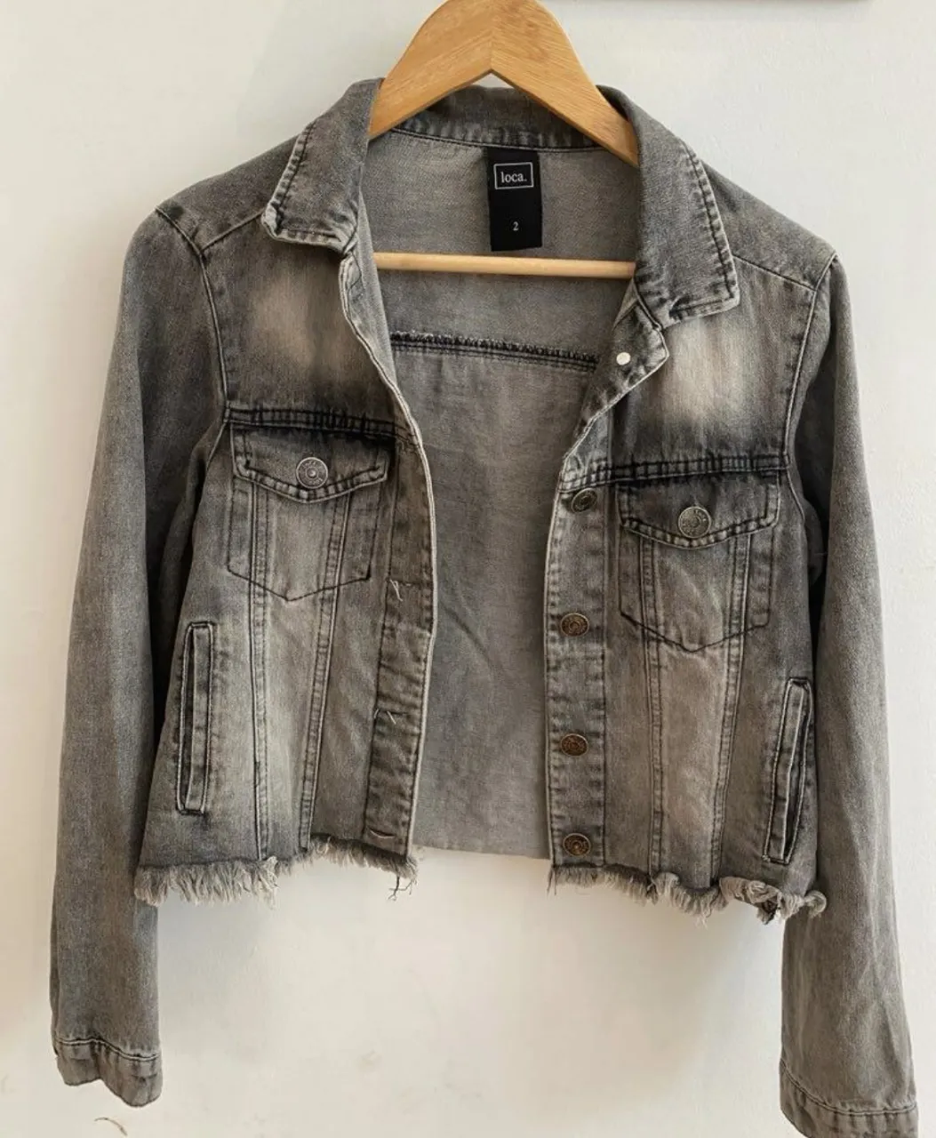 Campera de jean gris deslavado, con detalles de desgaste y flecos en el bajo. Talle 2 de la marca Loca. Ideal para un look casual y canchero.