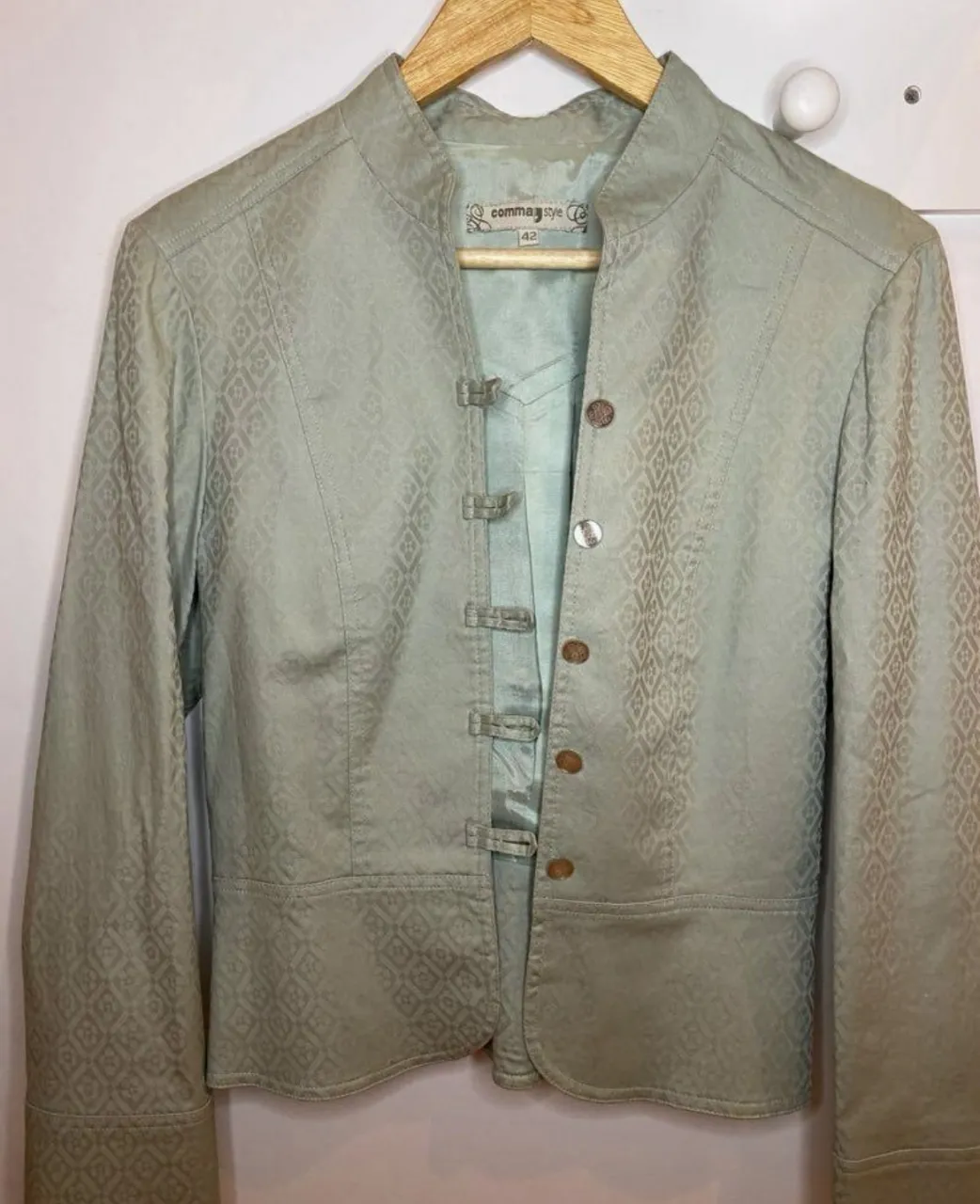 Chaqueta de mujer color verde claro con diseño en relieve. Tiene cuello mao, cierre con botones y detalles de diseño. Ideal para un look elegante y sofisticado.