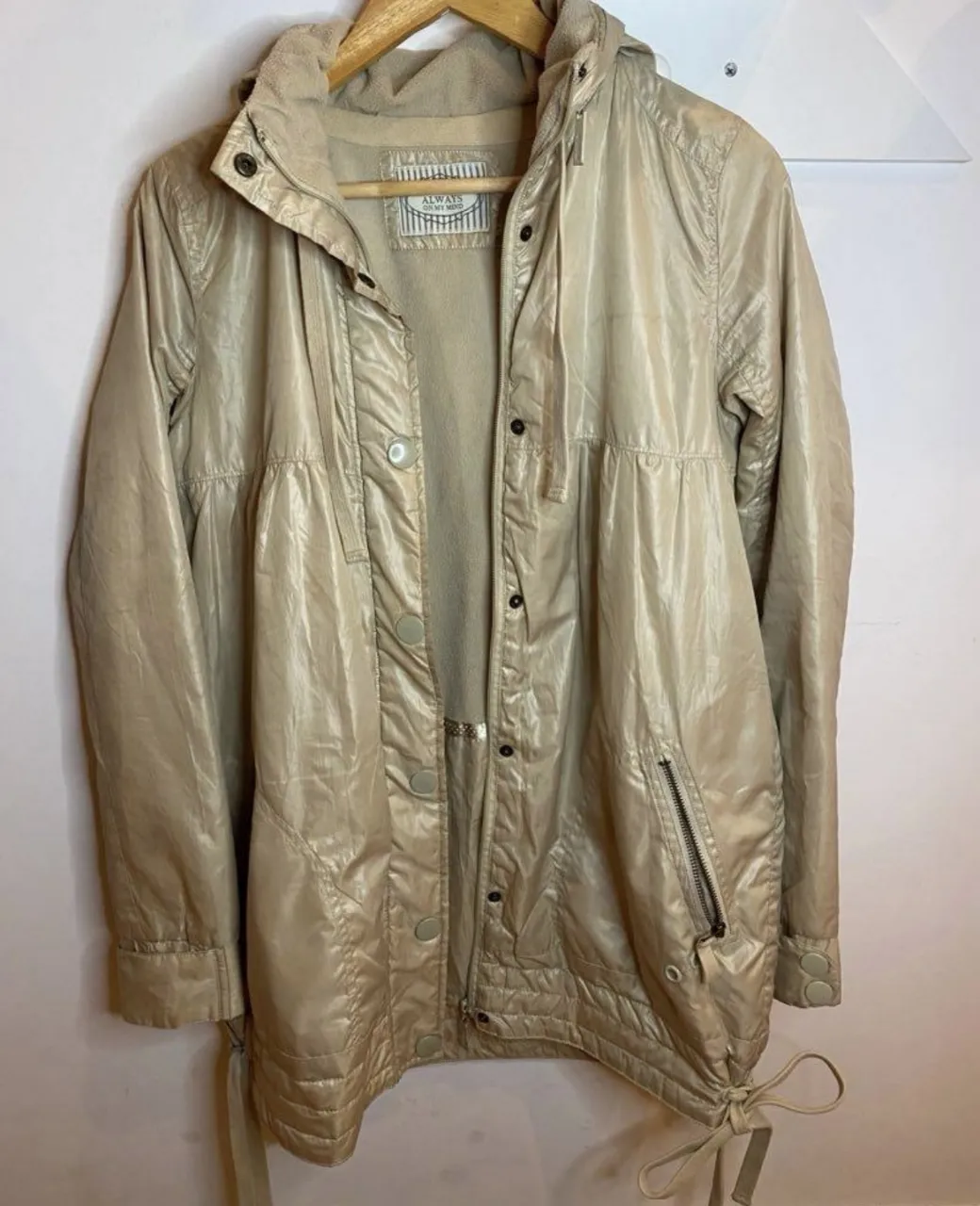 Campera deportiva beige con capucha, cierre y bolsillos. Talle 40. (para un s/m) es larga cubre la cintura y un poco más. Esta forrada por dentro, tiene polar en el interior y por fuera es rompe vientos. tiene capucha, se puede sacar y guardar. dos bolsillos con cierre afuera y uno adentro sin cierre. la tela es brillante en un color beige medio champagne.