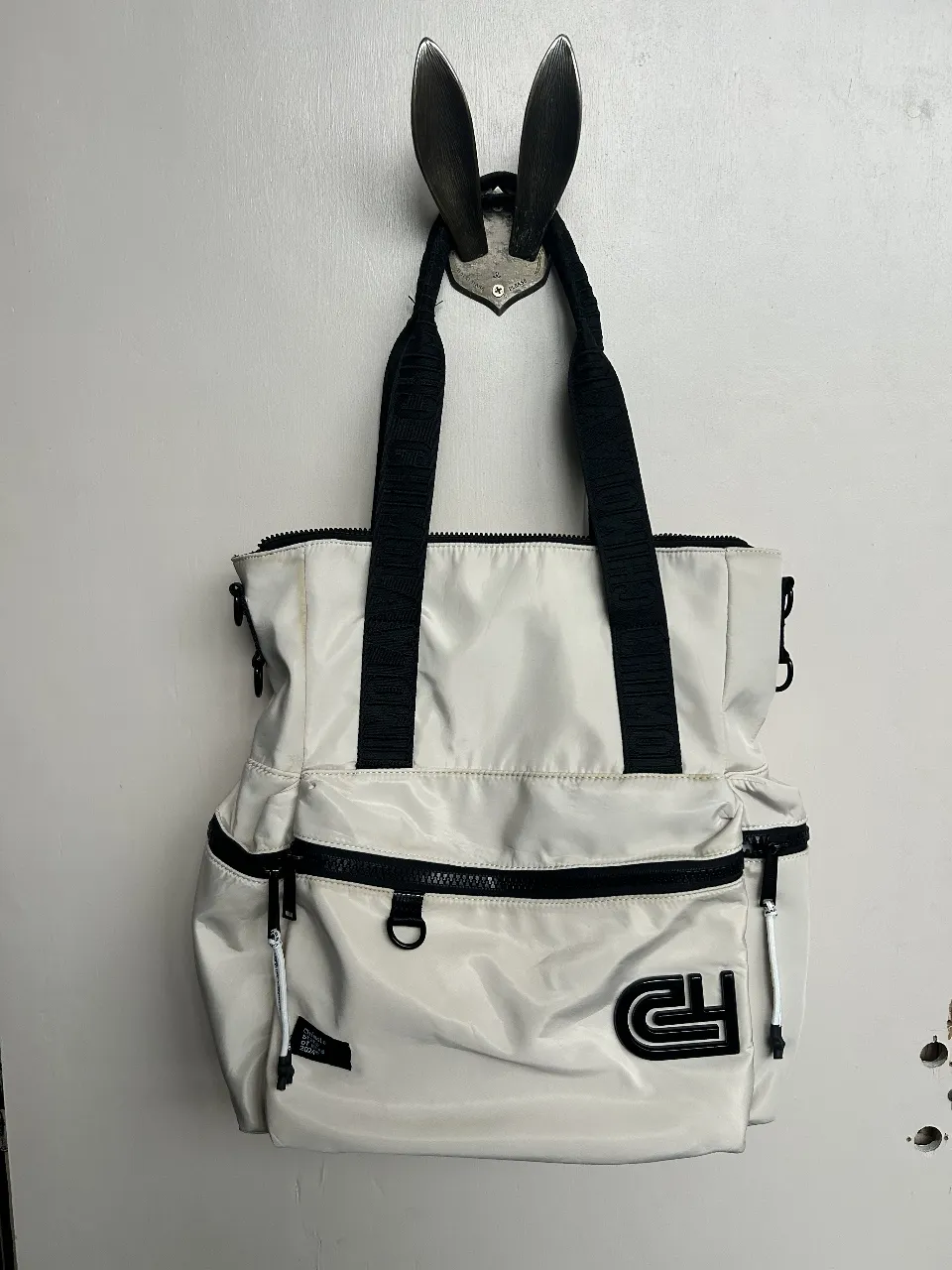 Bolso tote blanco con detalles en negro. Cuenta con cierre, múltiples bolsillos y el logo de la marca. Ideal para llevar todo lo que necesitas con estilo. Medidas: 40cm de alto x 36cm de ancho y 14cm de profundidad. Detalles en el color a la vista en las fotos, nada grave. todos sus cierres funcionan perfecto, hermosa calidad y súper amplio para llevar compu y mucho más. Ideal para el trabajo o la facu. 
