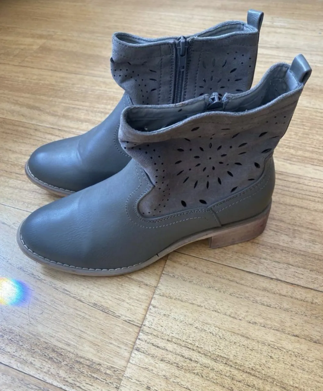Botas grises de mujer con detalles calados en la parte superior. Diseño moderno y versátil, ideales para combinar con diferentes outfits. Cierre con cremallera lateral para un ajuste fácil y rápido. 