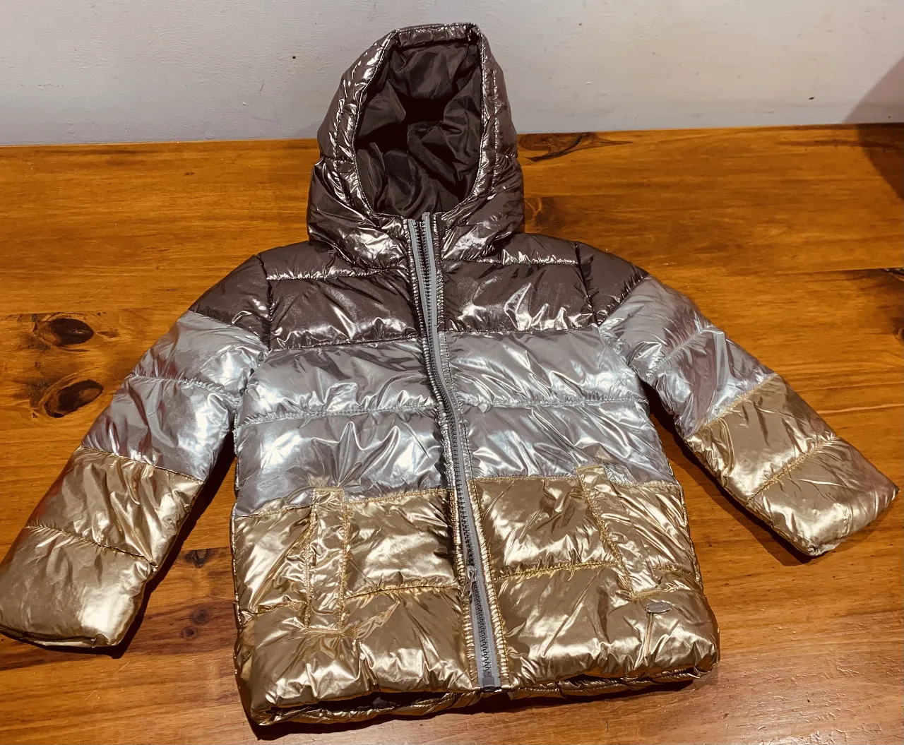 Campera acolchada para niña, con diseño metalizado en tonos dorado, plateado y marrón. Ideal para el invierno, con capucha y cierre.