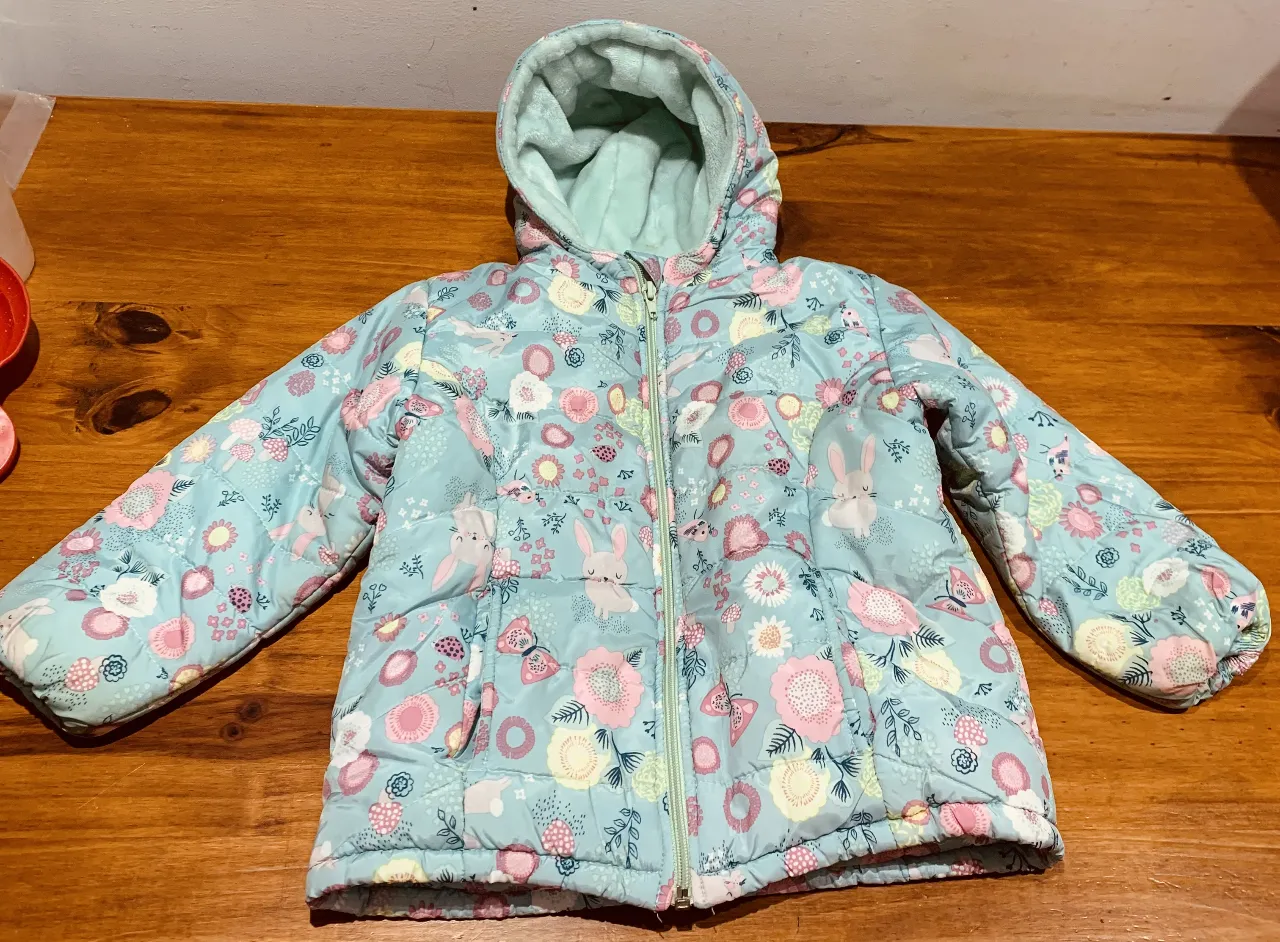 Campera acolchada para niña, con estampado floral y de conejitos. Posee capucha con forro de peluche y cierre frontal. Ideal para el invierno.