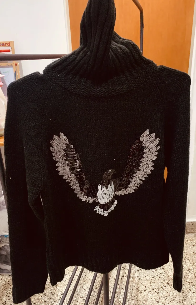 Sweater de cuello alto negro con diseño de águila plateada en la espalda. Ideal para un look moderno y abrigado.