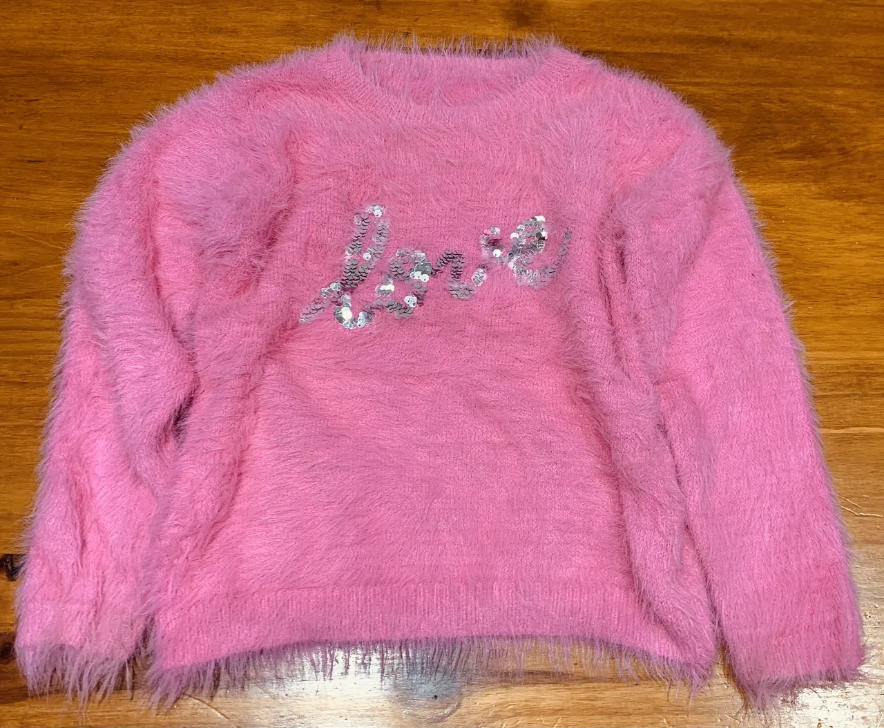 Sweater rosa peludo con la palabra "love" con lentejuelas. Ideal para un look casual y abrigado.