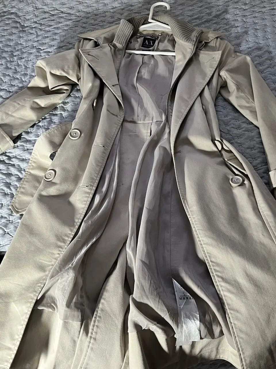 Trench coat beige de Armani Exchange, con cuello solapa y cierre con botones. Posee cinturón para ajustar en la cintura y bolsillos laterales. Ideal para un look elegante y sofisticado.