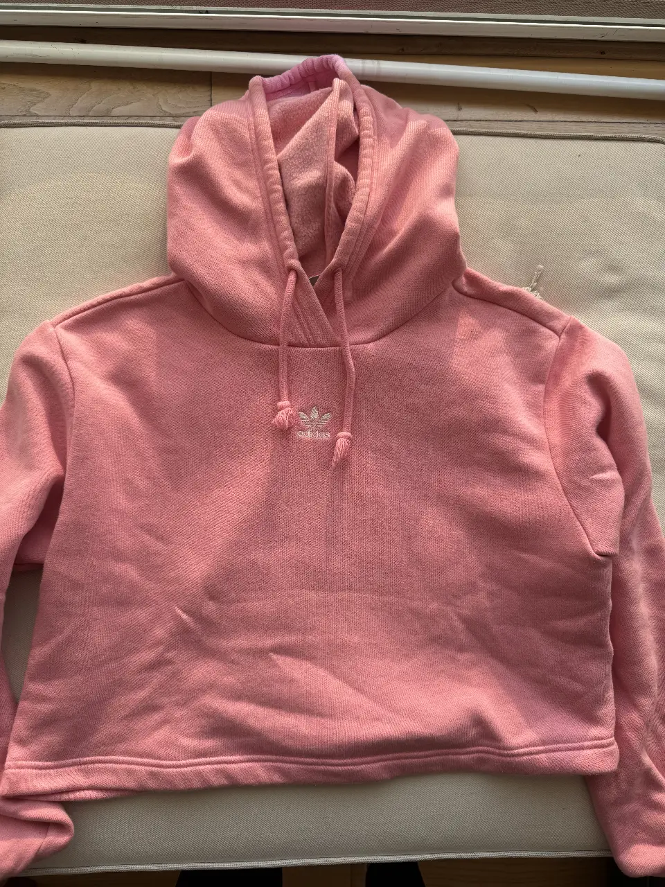 Buzo crop Adidas rosa, con capucha y el logo de la marca bordado en el pecho. Ideal para un look casual y deportivo.