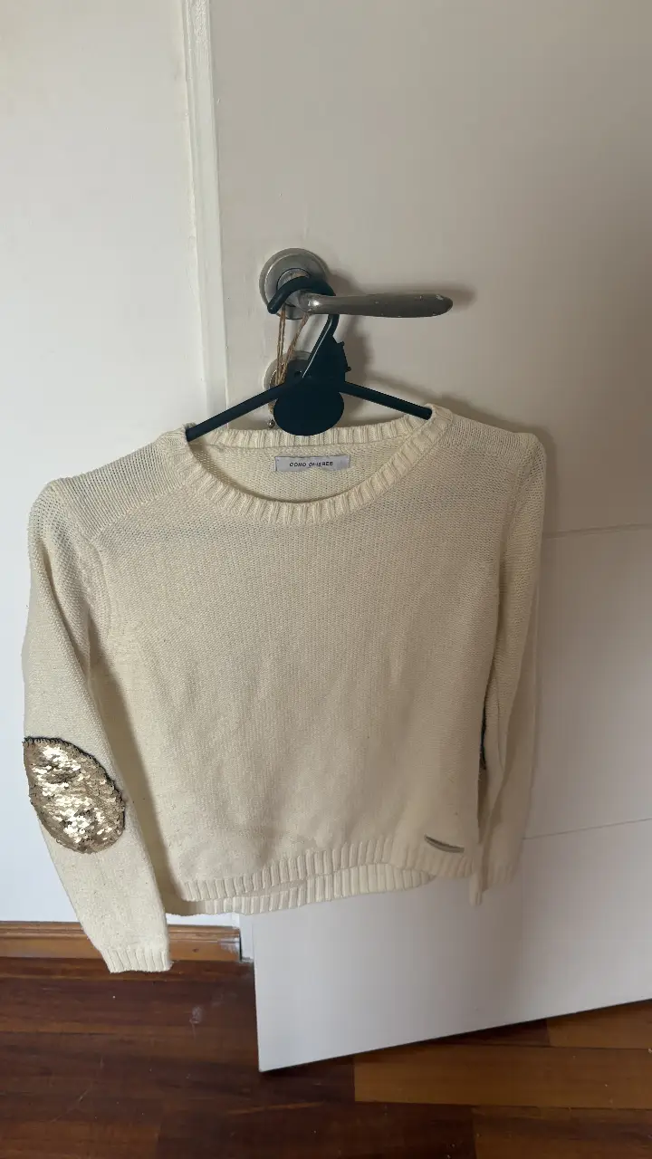 Sweater largo de color crudo con detalle de lentejuelas doradas en el codo. Ideal para un look casual y abrigado.