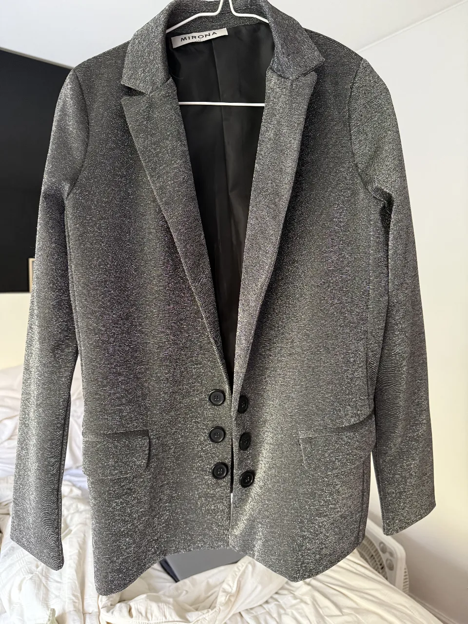 Blazer de mujer plateado con brillo, estilo elegante. Posee botones negros y bolsillos delanteros. Ideal para eventos formales o para darle un toque sofisticado a tu look diario. talle 42 