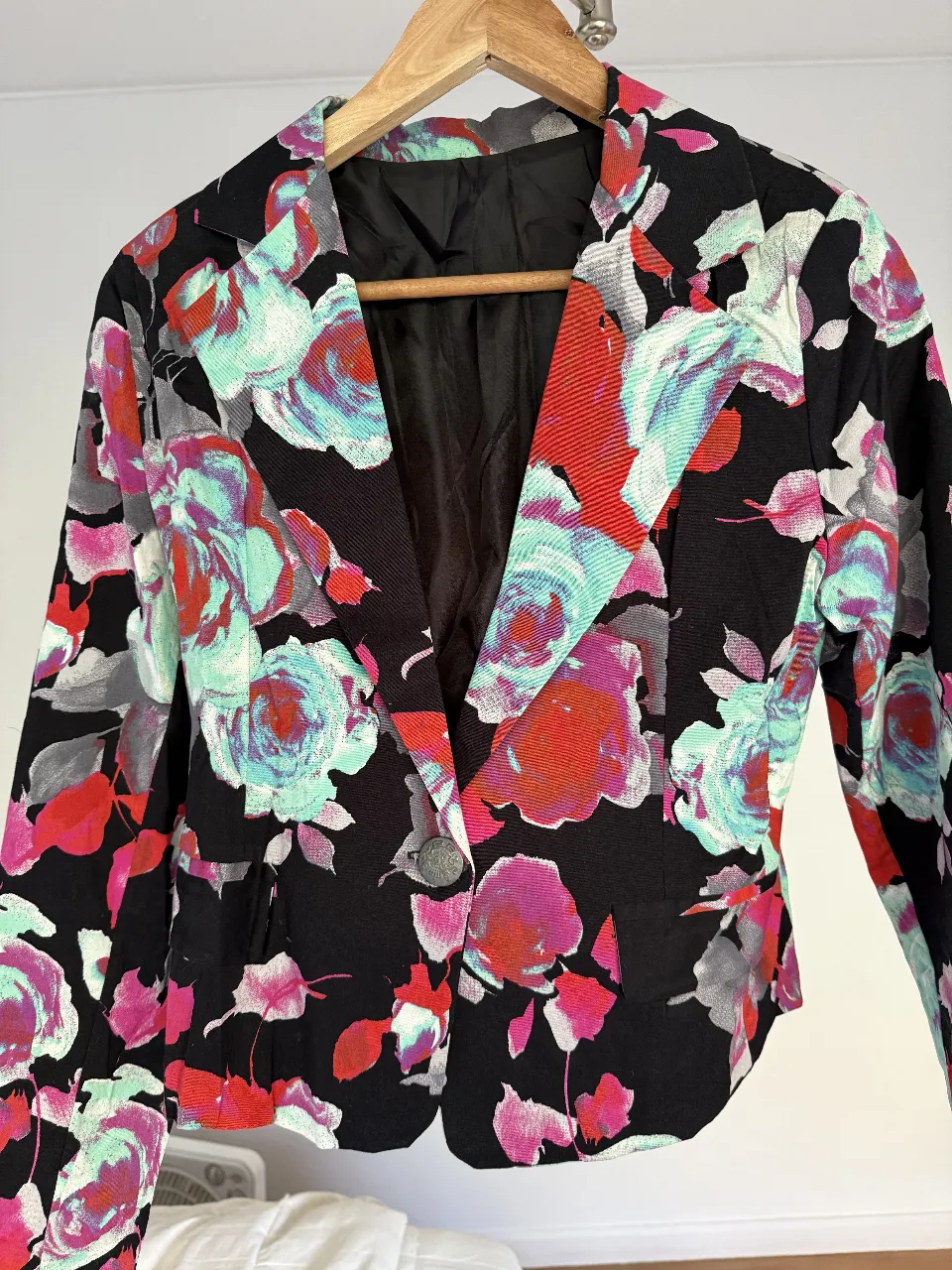 Blazer corto de mujer con estampado floral en tonos rojos, rosas y verde claro sobre fondo negro. Corte clásico con un botón y forro interior. Ideal para un look elegante y con estilo.