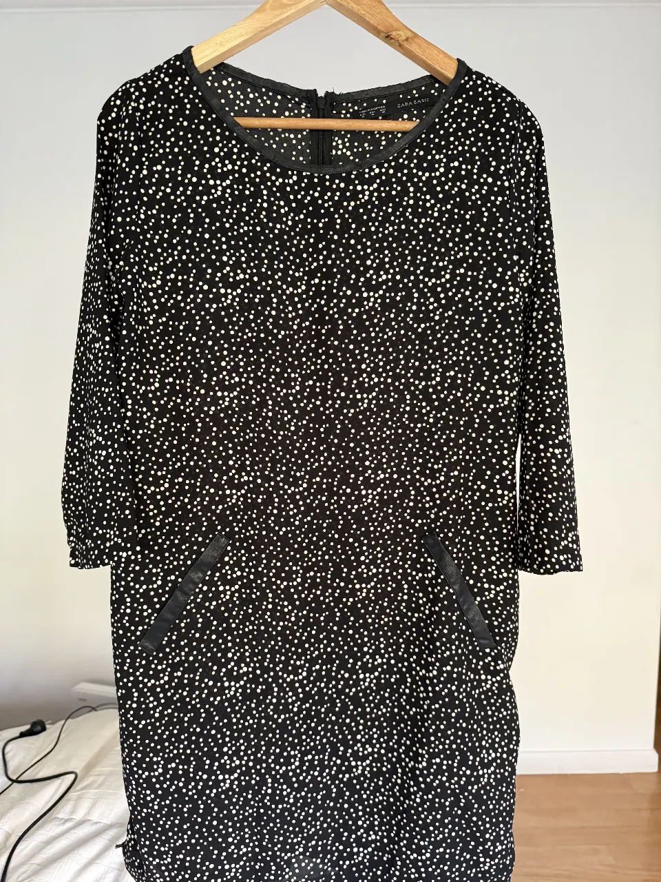 Vestido midi de Zara Basic con estampado de lunares blancos sobre fondo negro. Tiene mangas 3/4 y bolsillos delanteros. Ideal para un look casual y versátil.