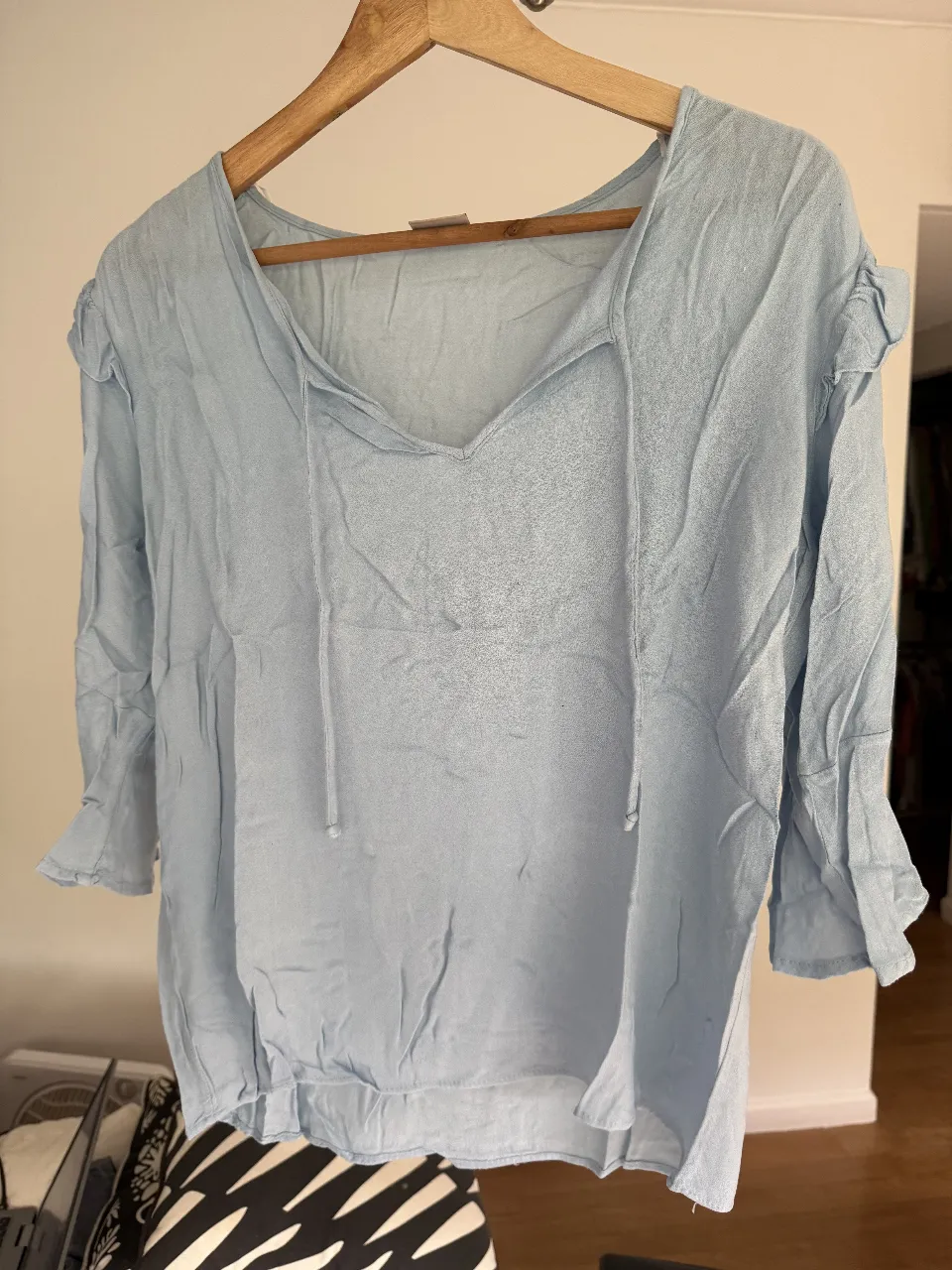 Blusa celeste con mangas 3/4 y detalles de volados en los hombros y mangas. Ideal para un look casual y fresco.