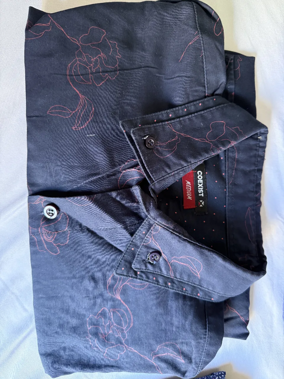 Camisa de hombre estampada en color azul marino con flores rojas. Cuello con botones y manga larga. Ideal para un look casual y moderno.