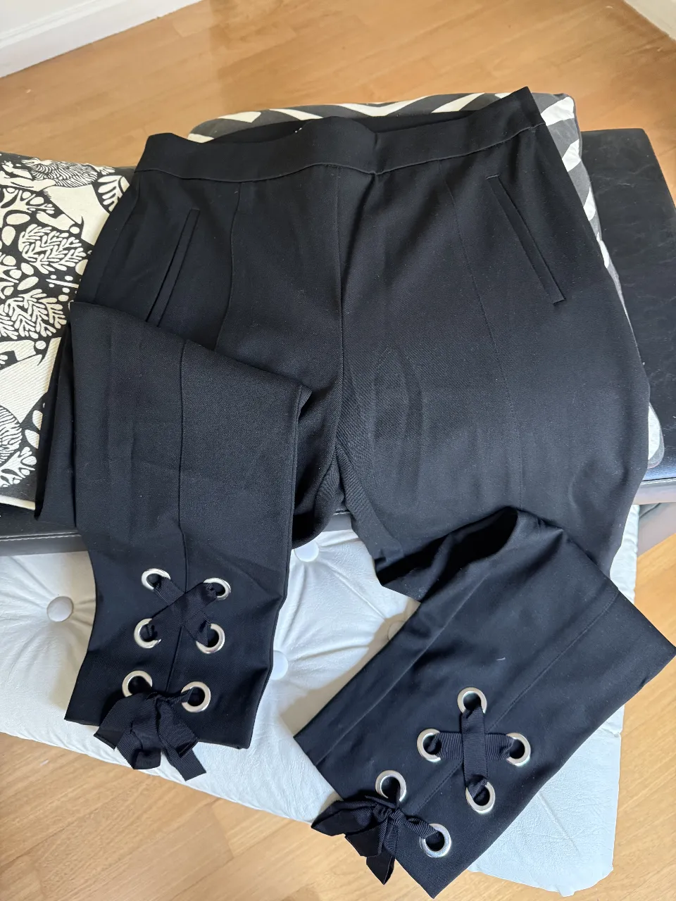 Pantalón tipo calza negro , elastizado y con cierre lateral , con detalles de ojalillos y lazos en los tobillos. Talle 38 de H&M. Ideal para un look elegante y moderno.