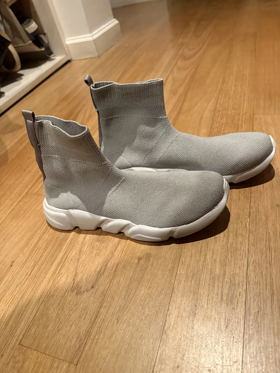 Zapatillas tipo botín de color gris, con suela blanca. Diseño moderno y cómodo, ideales para un look casual y urbano.  material tipo tejido elastico