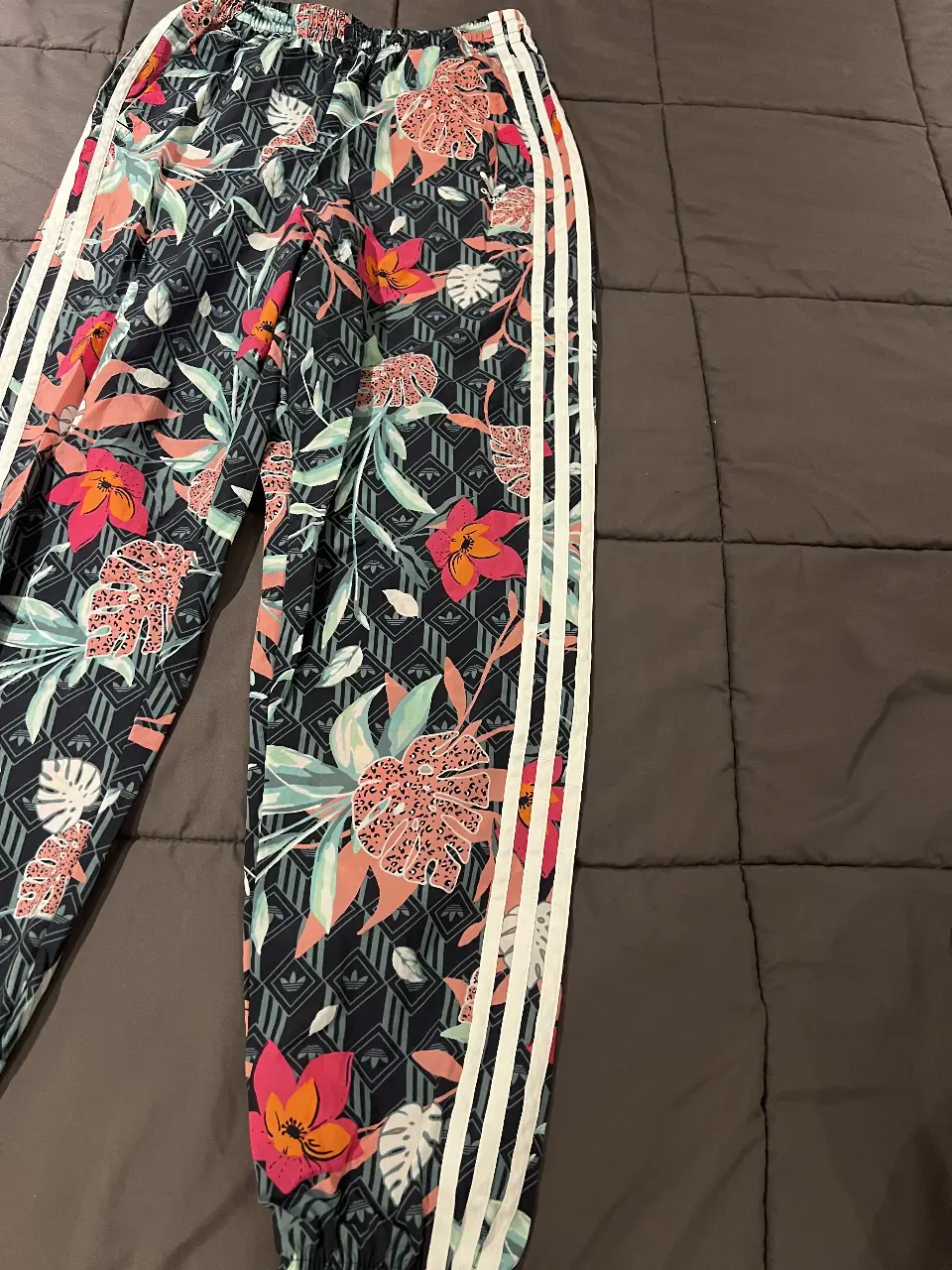 Pantalón Adidas estampado floral, tiro medio, con las clásicas tres tiras blancas a los costados. Ideal para un look casual y canchero.