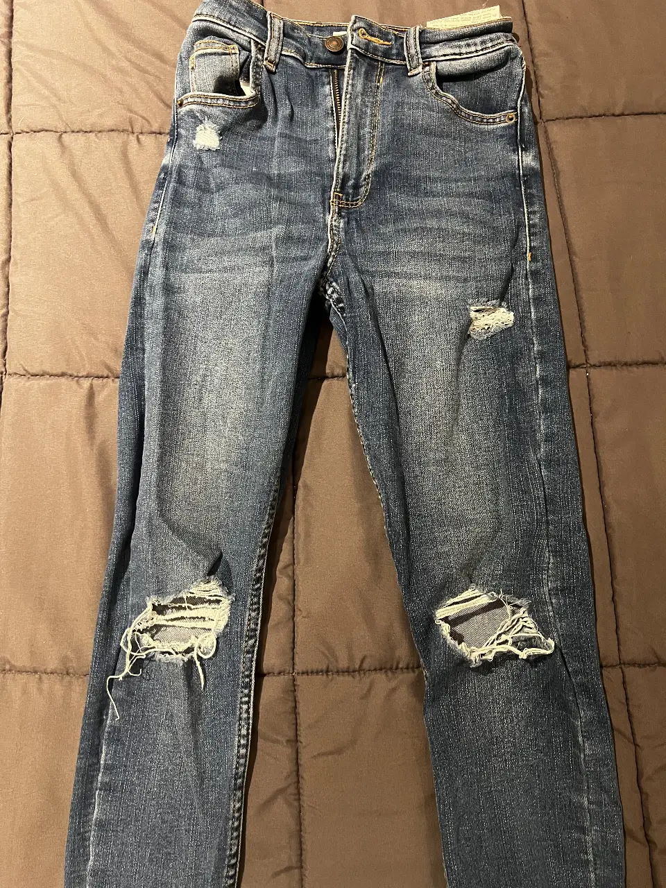 Jeans de hombre, azul gastado con roturas en las rodillas. Tiro medio, ideal para un look casual y moderno.