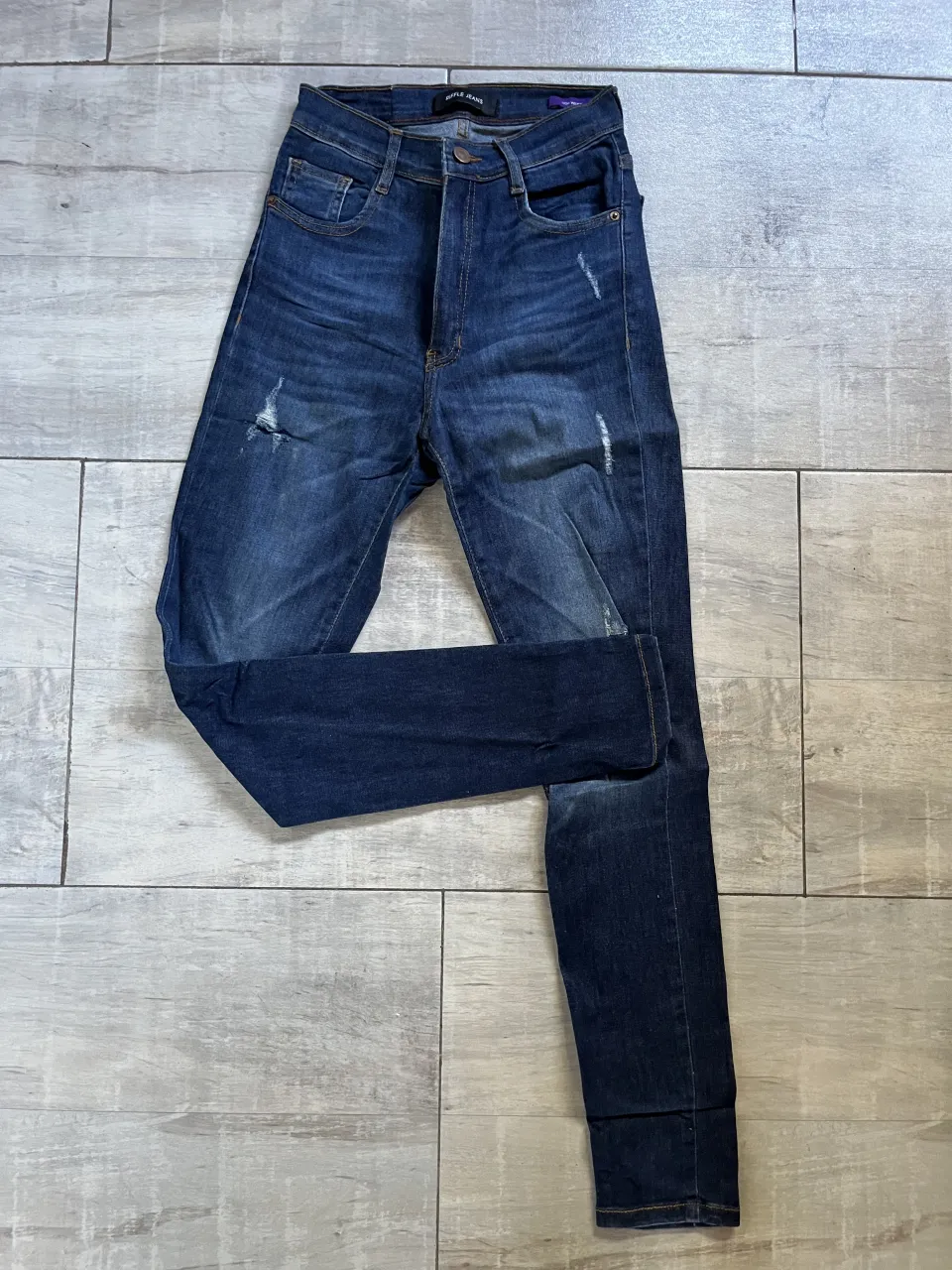 Jeans de mezclilla azul oscuro con roturas y desgastes.