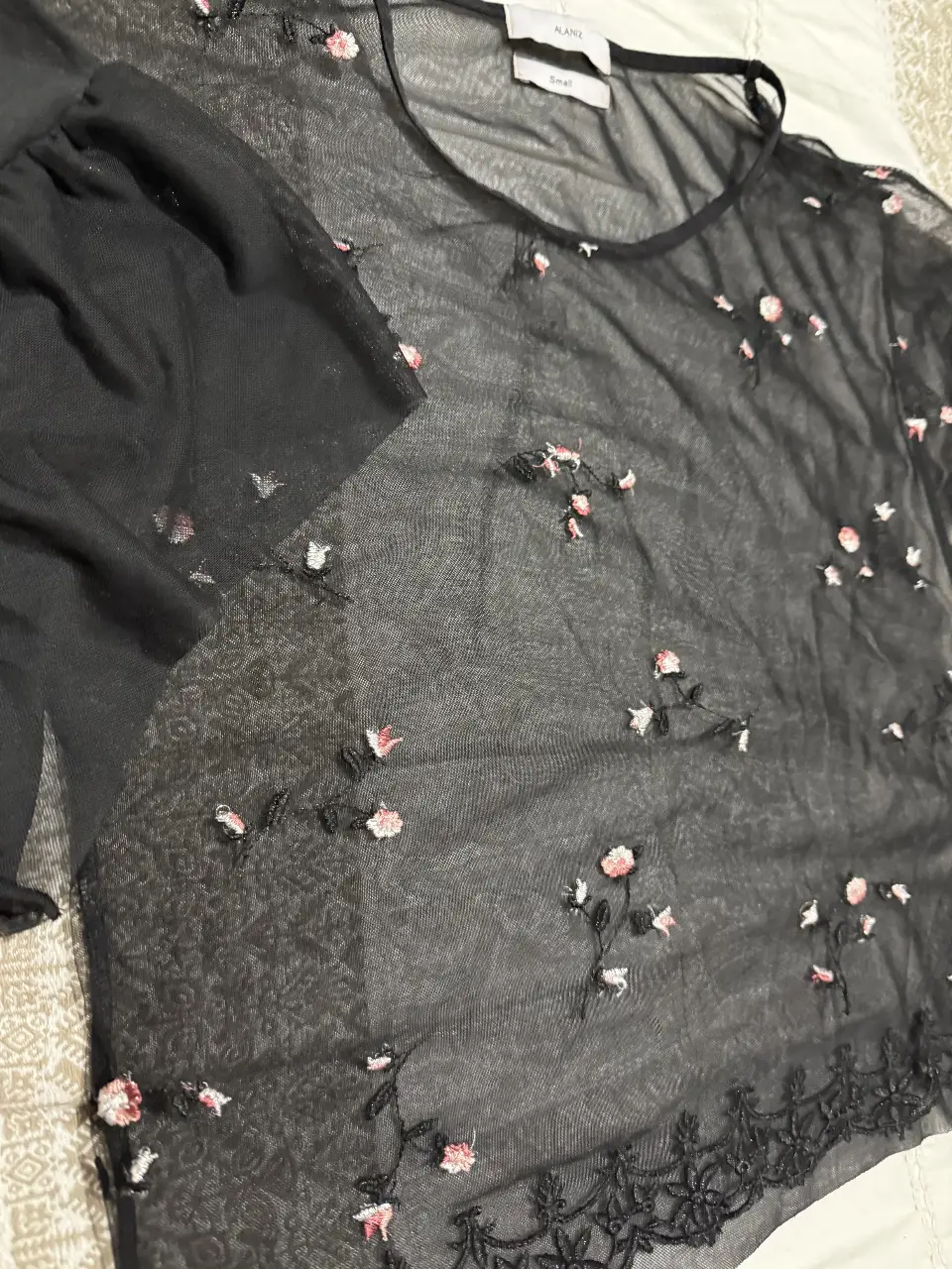 Blusa de red negra con bordados florales en tonos rosados y blancos. Ideal para un look elegante y sofisticado.