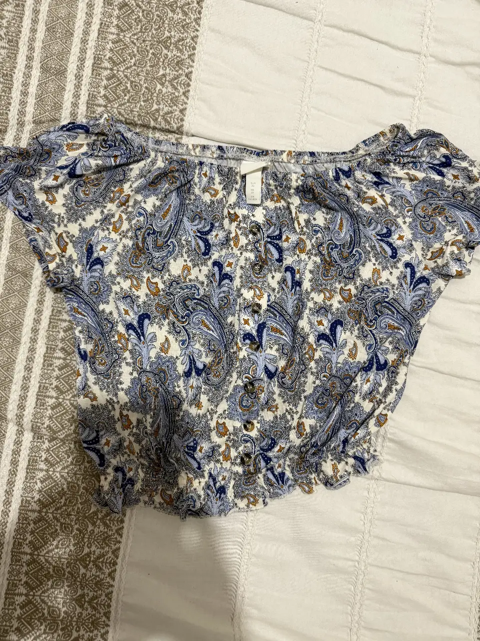 Blusa de mujer, cuello abierto (hombros) corta con estampado paisley en tonos azules y blancos. Diseño con mangas cortas abullonadas y detalle fruncido en la cintura. Ideal para un look casual y fresco.