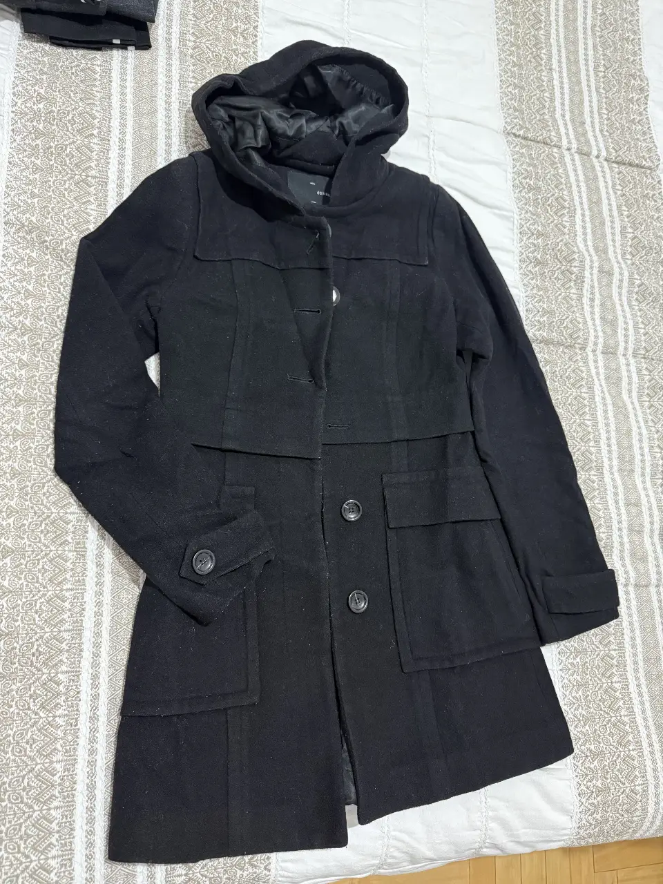 Tapado negro con capucha, ideal para el invierno. Cuenta con botones y bolsillos delanteros. Perfecto para un look casual y abrigado. con pelotitas del uso